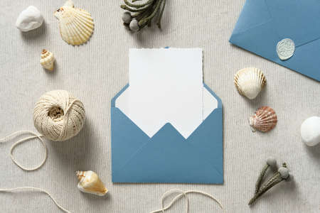 Wedding envelope with invitation card mockup inside and seashells on table. Sea, nautical style wedding concept.の写真素材