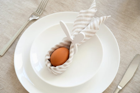 Easter egg with rabbit ears made of napkin on white plate