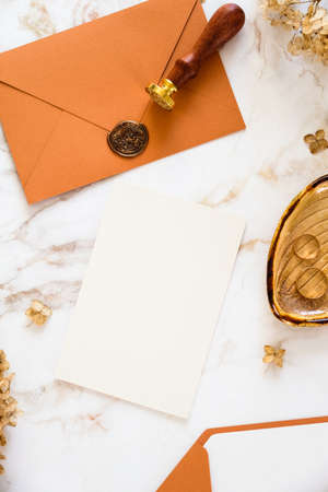Autumn still life wedding stationery set. Blank paper card, orange envelope, golden rings, dried flowers on marble background.の写真素材