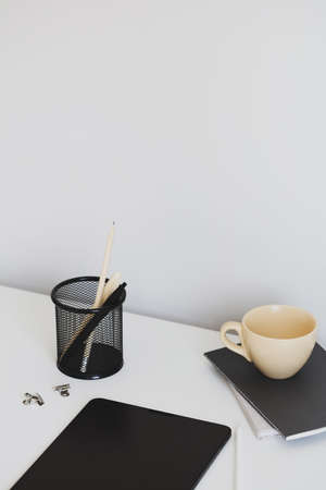Modern home office desk table with stationery, black notebooks, tablet, cup of coffee. elegant style.の写真素材