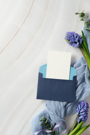 Blue envelope with blank card on a marble background, surrounded by purple hyacinth flowers and a light blue fabric. Ideal for wedding invitations, greetings, or announcements. Flat lay, top viewの写真素材
