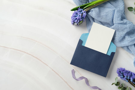 Navy blue envelope with blank paper card, purple hyacinth flowers on a marble desk with a light blue fabric. Elegant wedding invitation card template. Flat lay, top view, copy spaceの写真素材