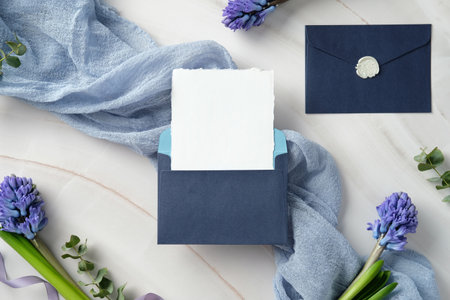 Elegant navy blue envelope with a blank card, surrounded by purple hyacinth flowers and a light blue fabric, perfect for wedding invitations, greeting cards, or special announcementsの写真素材
