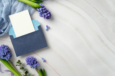 Blue envelope with blank card and purple hyacinth flowers on marble background. Ideal for wedding invitations, greetings, or announcementsの写真素材