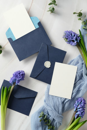 Luxury wedding stationery set. Elegant navy blue envelopes with blank cards, adorned with a wax seal, surrounded by purple hyacinth flowers and eucalyptus leaves on a marble deskの写真素材