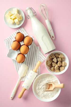 Baking essentials on a pink background: eggs, butter, milk, flour, brown sugar, whisk, rolling pin, and spatula. Ideal for food blogs, recipes, and culinary contentの写真素材