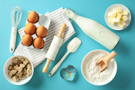 Baking ingredients and tools on a blue background, including eggs, flour, butter, milk, a rolling pin, and cookie cutter. Flat lay, top viewの写真素材
