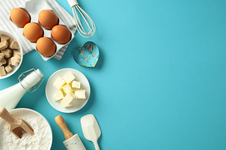 Baking essentials on a blue background: eggs, butter, milk, flour, sugar, whisk, spatula, and colorful sprinkles. Flat lay, top viewの写真素材