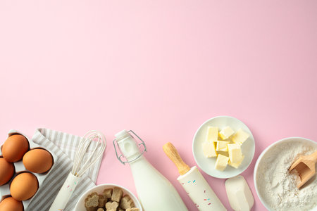 Top view baking ingredients and tools on a pastel pink background, including eggs, butter, flour, sugar cubes, a rolling pin, and a milk bottleの写真素材