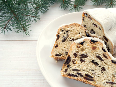 Stollen German Christmas cake on the white plate and blue spruce branches on the whitewooden planks