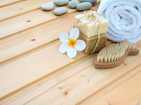 White rolled towel, tiare flower, soap tied with jute rope, stones and fish shaped nail brush on the wooden planksの写真素材