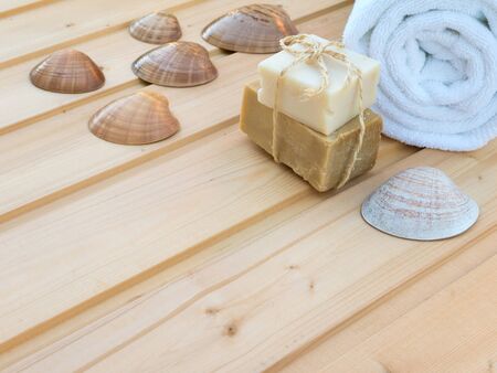 White rolled towel, soap bars tied with jute rope and seashells on the wooden planksの写真素材