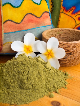 Henna powder in the coconut bowl and two tiare flowers on the colorful pillows backgroundの写真素材