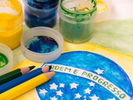 Paint in jars, lids and pencils on the brazil flag watercolor painting. Inscription on the flag "Ordem e Progresso" (portuguese "Order and Progress").の写真素材