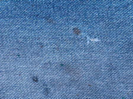 Old faded light blue denim with spots and hole backgroundの写真素材