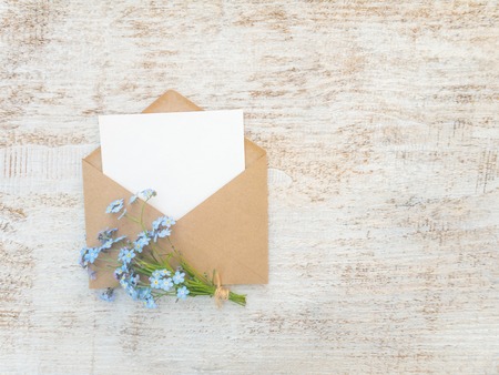 Brown paper envelope with white blank card and blue forget-me-not flowers 
bouquet tied with jute rope on the rustic white painted backgroundの写真素材