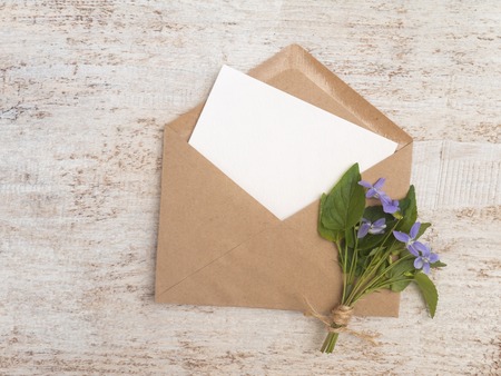 Brown paper envelope with white blank card and wild viola flowers bouquet tied with jute rope on the rustic white painted backgroundの写真素材