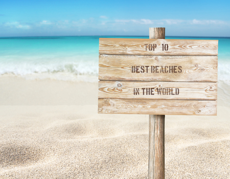 Top ten beaches in the world message on the wooden planks sign board on the beach blurred background. 
Tropical island paradise. Sandy shore washing by the wave. Bright turquoise ocean water.の写真素材