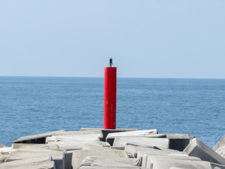 Red lighthouse on the pier of concrete blocks at the port entrance. Navigation sign. Channel marker in Puerto de Vega, Asturias,Spain.の写真素材