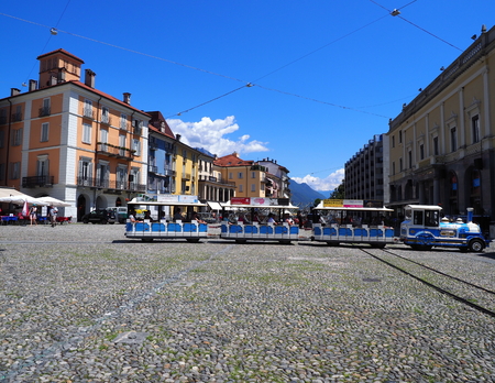 Small tourist train, colorful buildings on Piazza Grande main Locarno city square in Switzerlandのeditorial素材