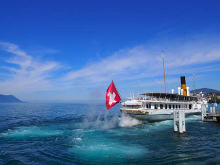 MONTREUX, SWITZERLAND on JULY 2017: Paddle-wheel steam boat sails away at promenade on Leman Lake in european city in canton Vaud, clear blue sky in warm sunny summer day.のeditorial素材
