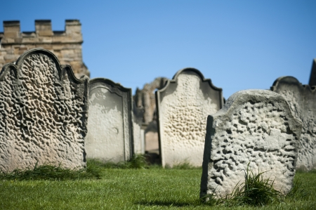Old weathered gravestones arranged haphazardly on green grass, closeup view against a blue skyの写真素材