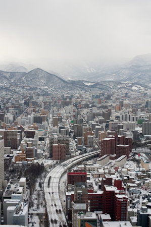 View from above down towards highway and buildings in Sapporo, Japan under overcast winter skiesの写真素材