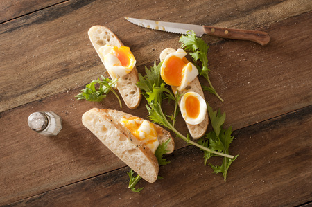 Soft cooked eggs sliced and served on bread beside long stemmed herbs and a serrated knifeの写真素材