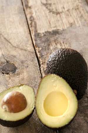 Ripe halved and whole avocado pear on a rustic wooden table ready to be served as a salad ingredient, high angle view with copy spaceの写真素材