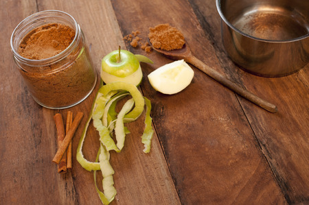 Fresh half peeled apple with aromatic cinnamon spice in the form of sticks and ground powder for use as a flavoring and seasoning in baking on a wooden kitchen table with copy spaceの写真素材