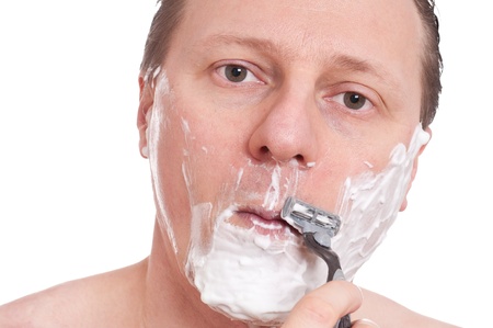 A caucasian with shaving foam in his face is shaving with a razorの写真素材