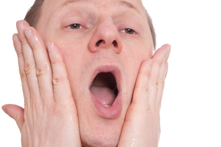 A man with open mouth is rubbing aftershave on his cheeks and it aches