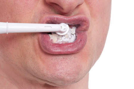 An electric toothbrush is cleaning the male teeth