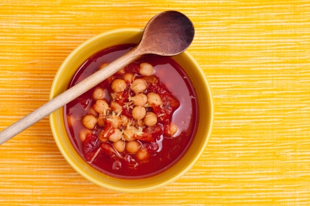 Soup peas and tomatoes in a yellow bowl with wooden spoonの写真素材