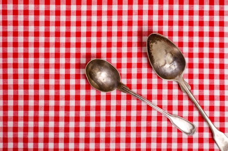 Two old silver spoons on a red and white checked table clothの写真素材