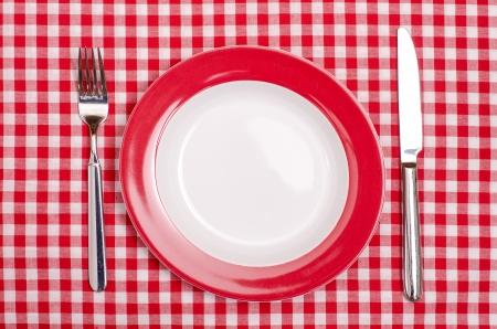 Plate with fork and knife on a red and white checked table clothの写真素材