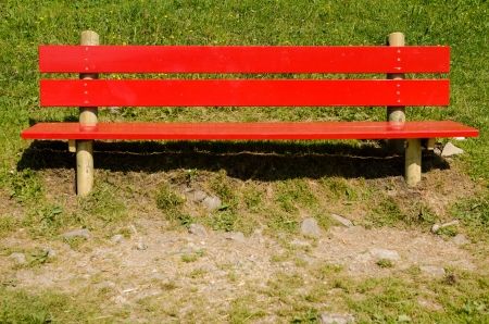 Bright red bench on a green meadow with pebbly foregroundの写真素材