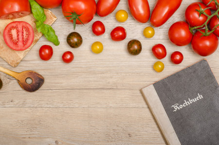 Different tomatoes with wooden spoon and recipe book on a old wooden boardの写真素材