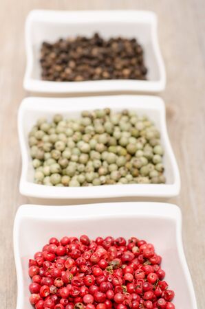 Different pepper in red, green and black in white porcelain bowlsの写真素材