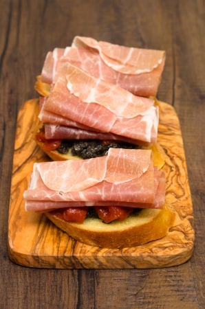 Bread with olive paste, tomatoes and parma ham as snack in vertical formatの写真素材