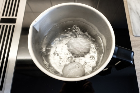 Boiling eggs in a stainless steel pot on a stove with steam extractorの写真素材