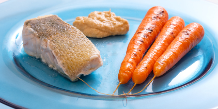 Zander fish filet roasted with carrots and hummus on blue plateの写真素材