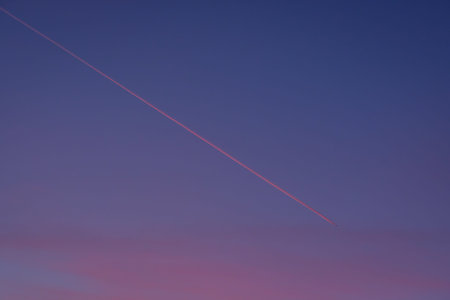 Airplane with condensation trail in blue sky dawn