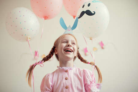 Pretty little girl in a pink dress and cap Bunny rabbit with balloons on the pigtails laughs. Childhood. Easter. The occasion.の写真素材