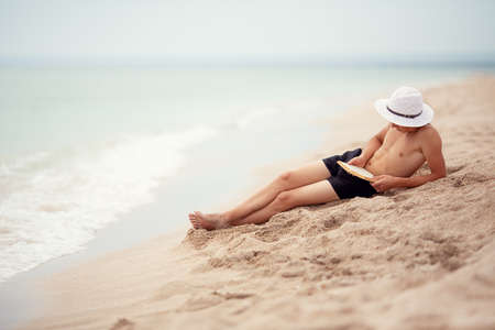 A teenager reads a book on the beach.の写真素材