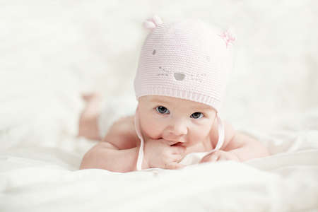 Newborn baby girl in pink knitted hat on a bed.の写真素材