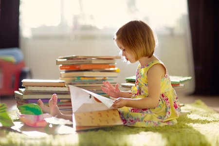 A little cute girl in a yellow dress reading a book sitting on the floor