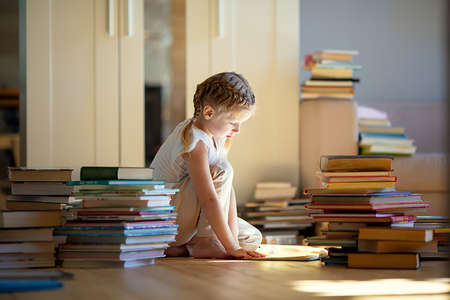 A little cute girl in a yellow dress reading a book sitting on the floorの写真素材