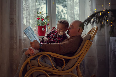 grandfather sitting in a chair and reading a fairy tale to his granddaughter on Christmas eve