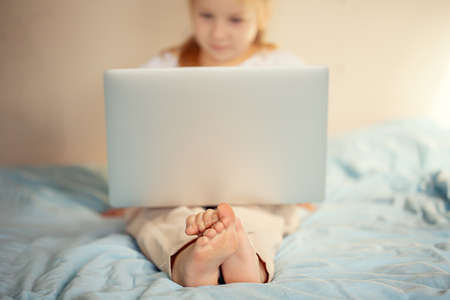 A cute girl sitting on the bed is watching something on a laptop. The concept of educationの写真素材